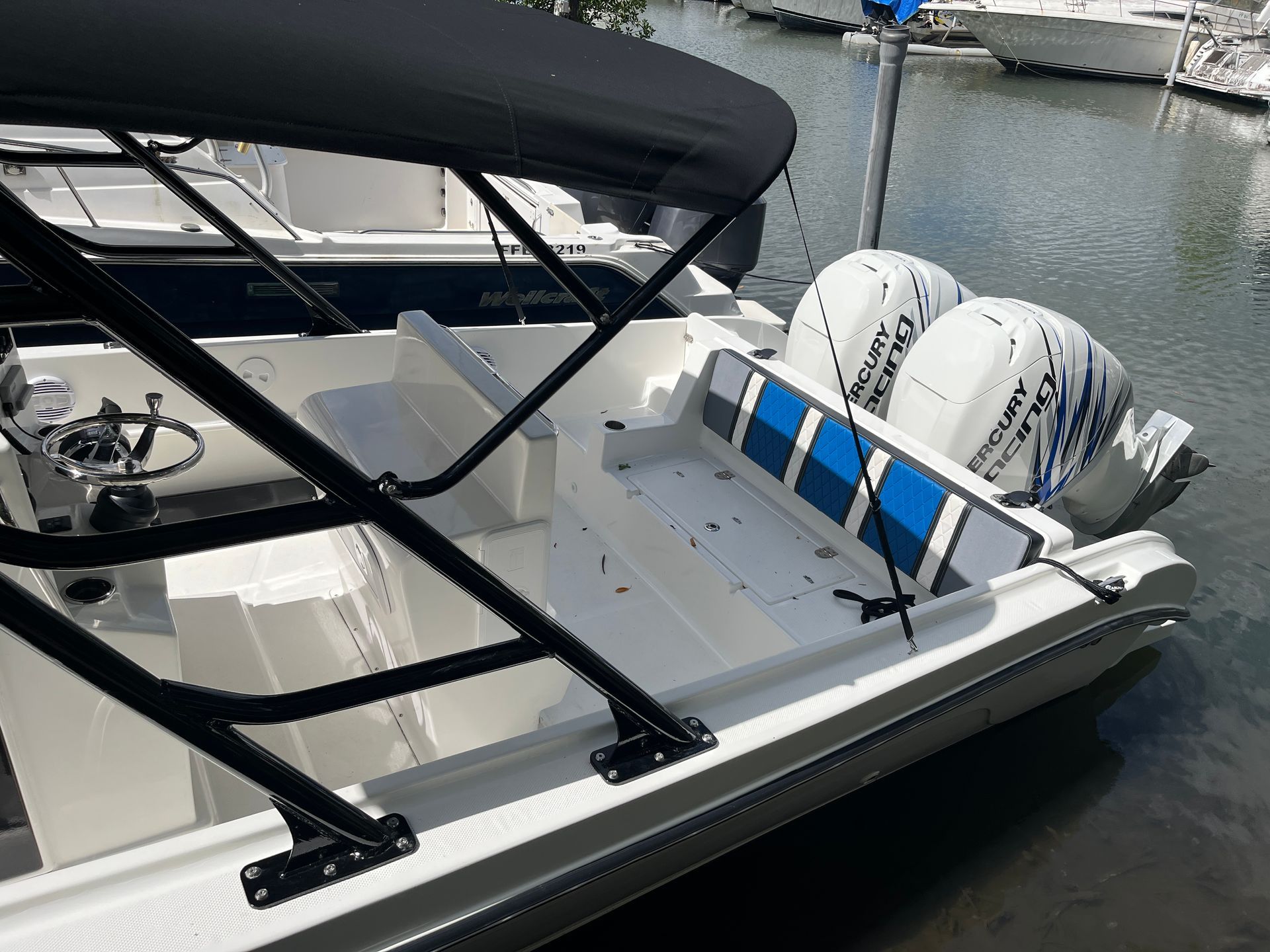 Cockpit d'un bateau avec capote noire, sièges bleus et deux moteurs hors-bord dans une marina