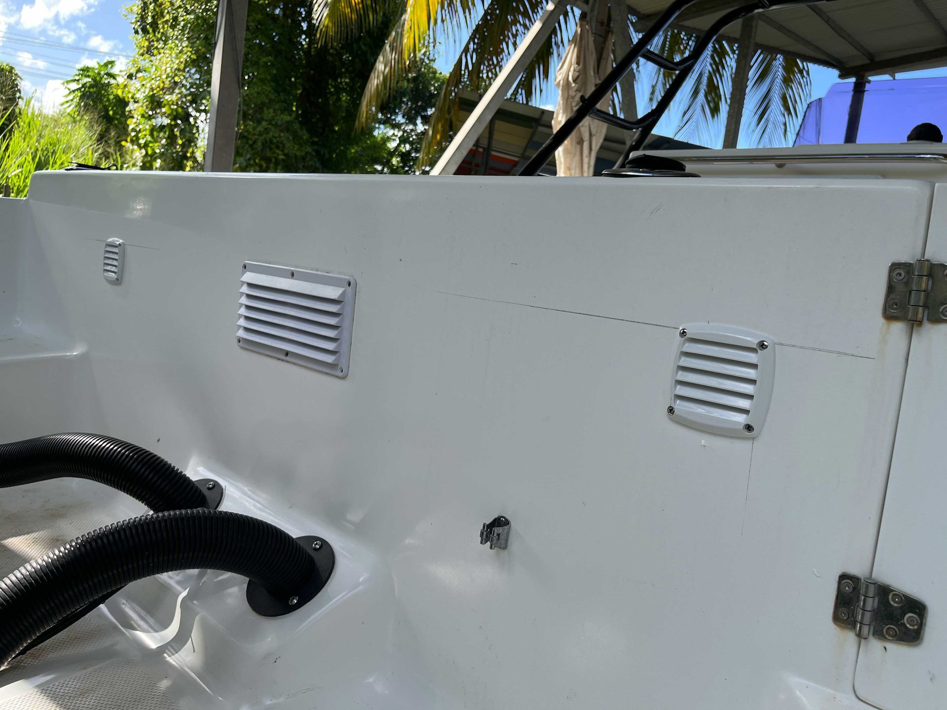 Coque de bateau en fibre de verre blanche avec aérations et tuyaux noirs dans un environnement extérieur ensoleillé