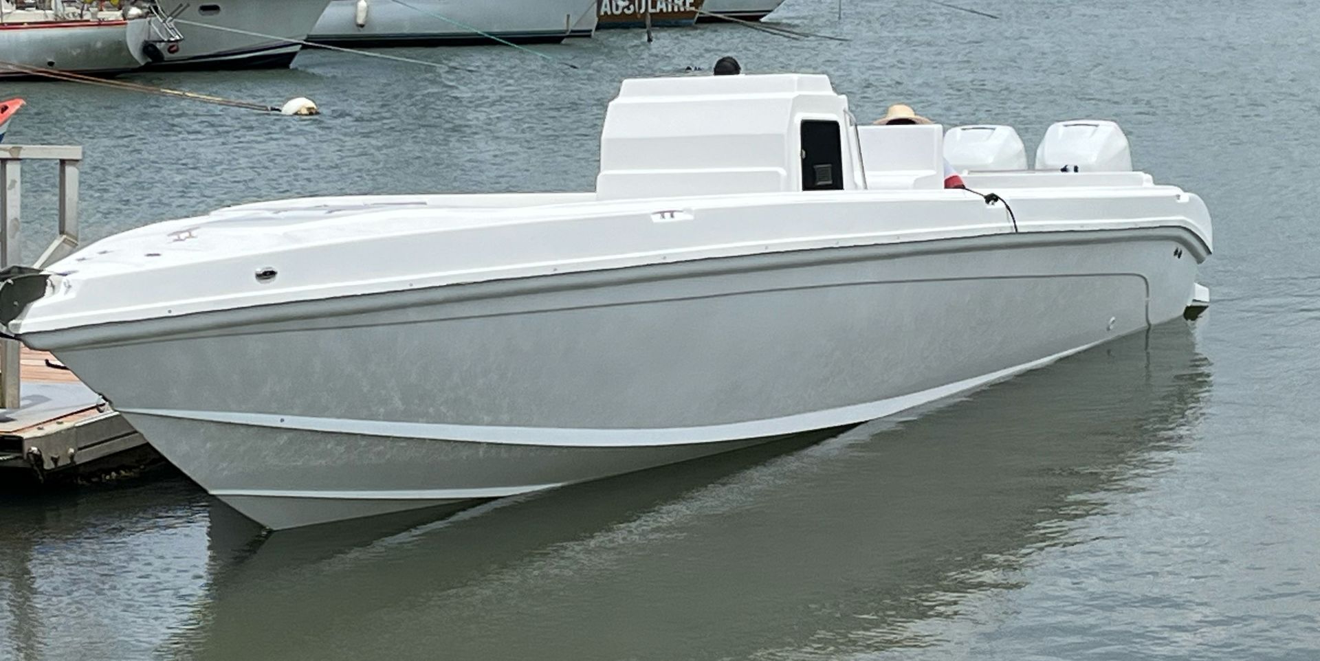 Un hors-bord blanc amarré sur une eau calme à côté d'un port de plaisance, vu de côté.