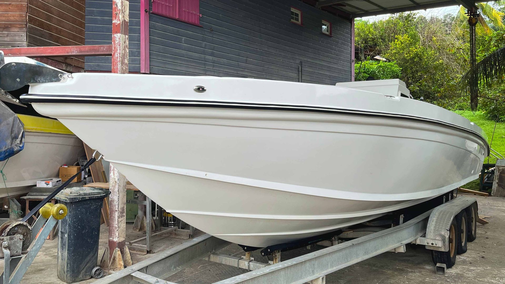 Bateau blanc sur une remorque sous un abri, stationné à côté d'un bâtiment.