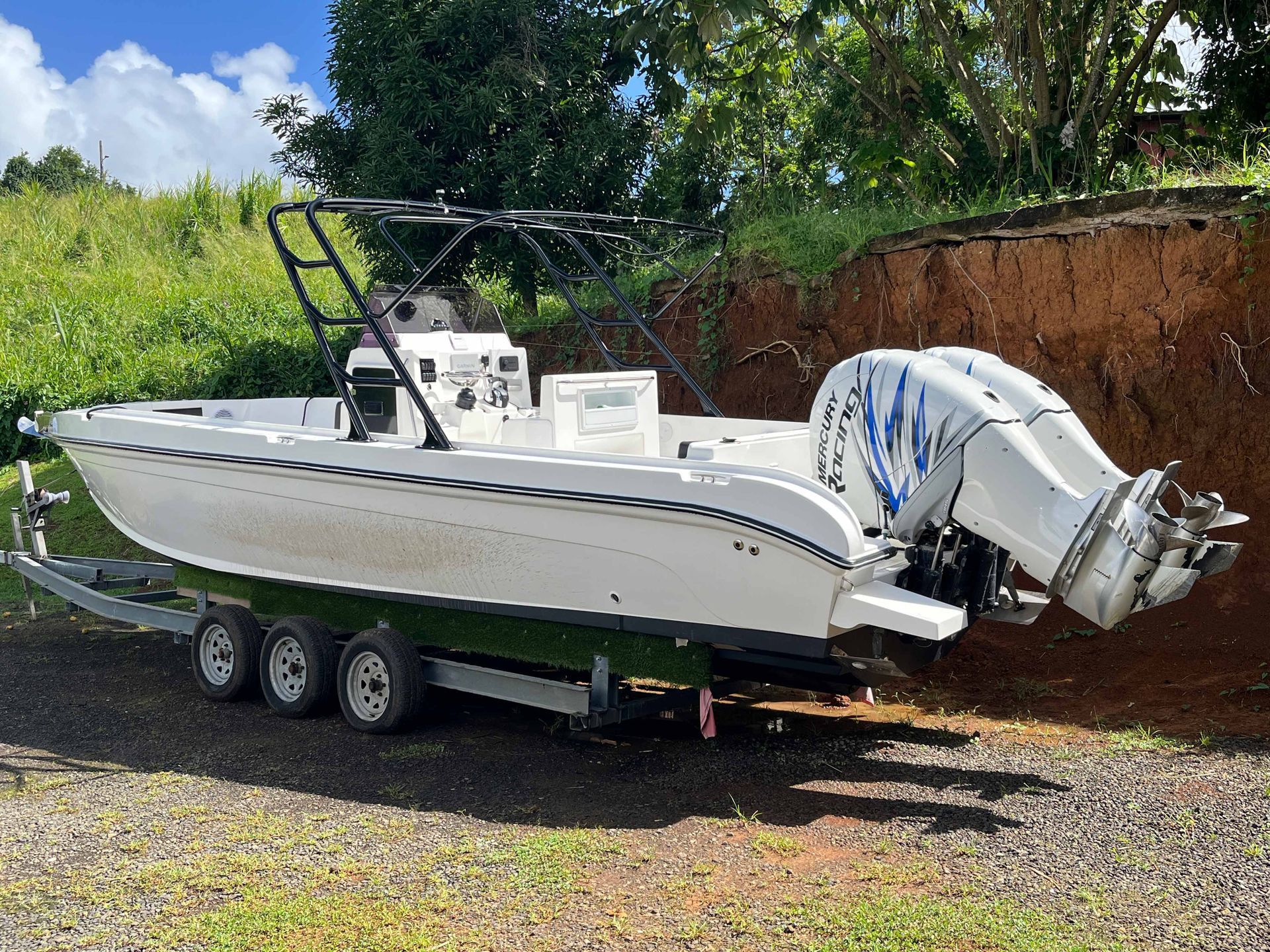 Bateau blanc à console centrale sur une remorque avec moteur hors-bord, stationné sur du gravier près d'un talus de terre.