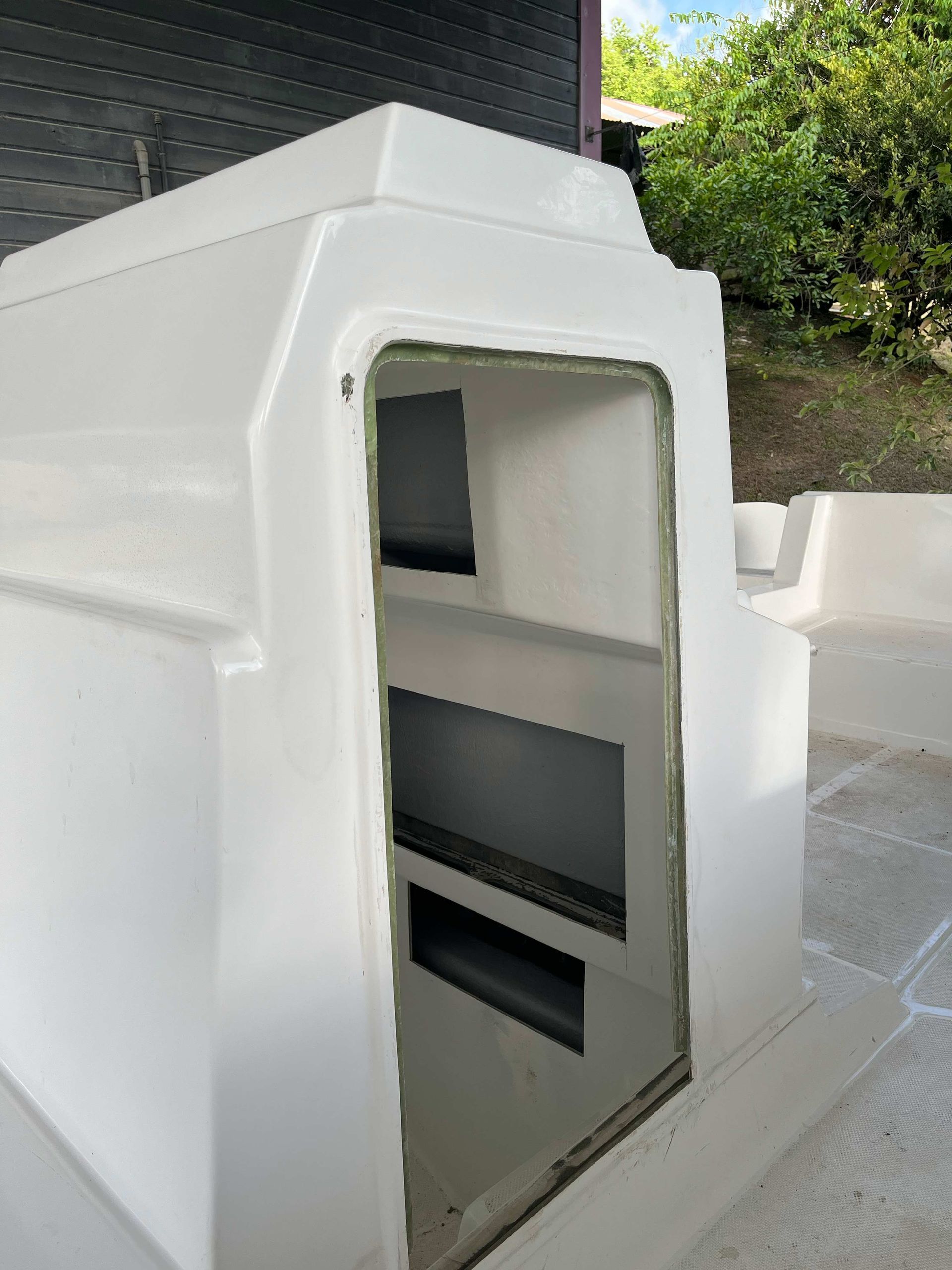 Enclos extérieur rectangulaire blanc à façade ouverte, laissant apparaître une étagère intérieure sombre sur fond de patio.
