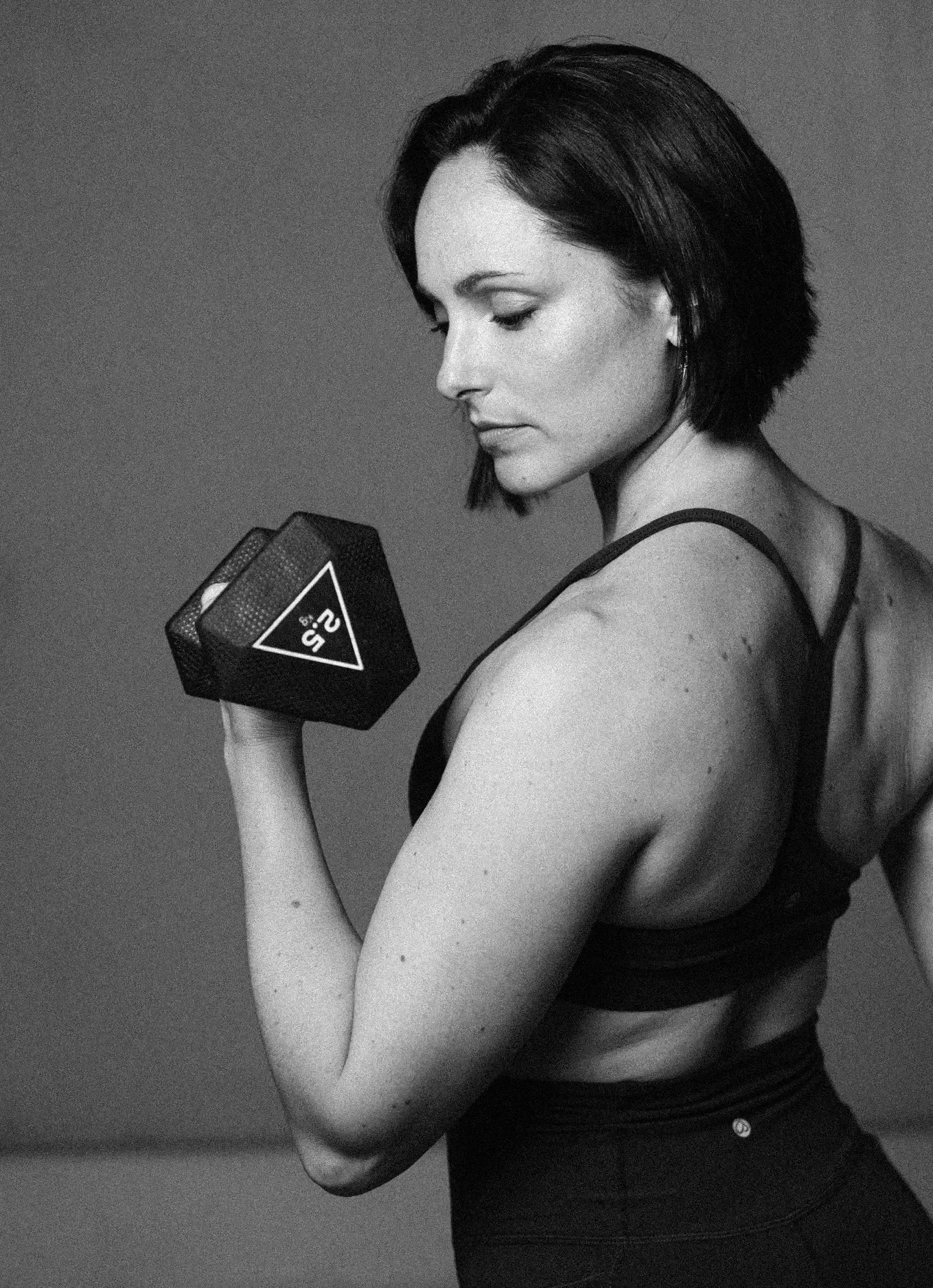 Woman in workout clothes, flexing a dumbbell.