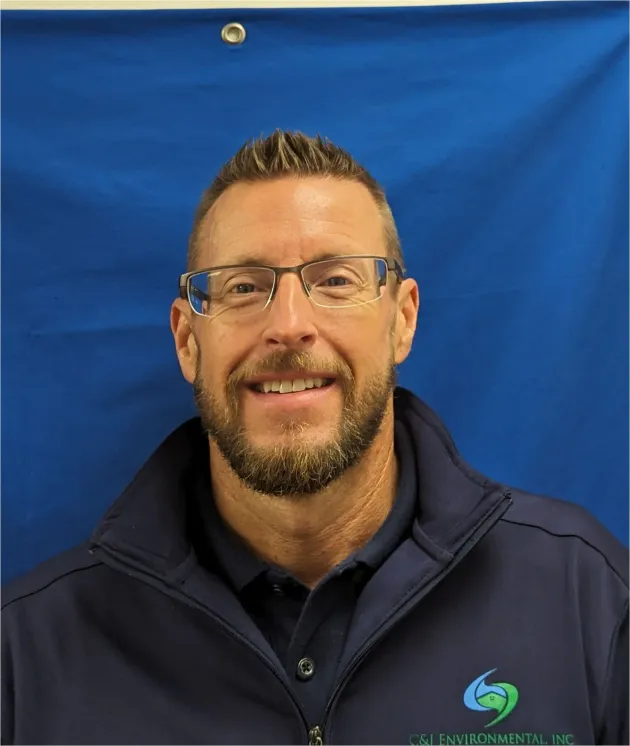 A man with glasses and a beard is smiling in front of a blue background