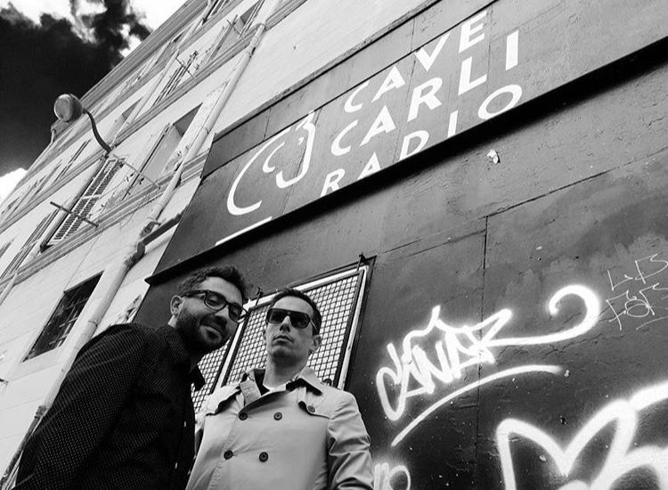 Two men standing in front of a building that says cave carli radio