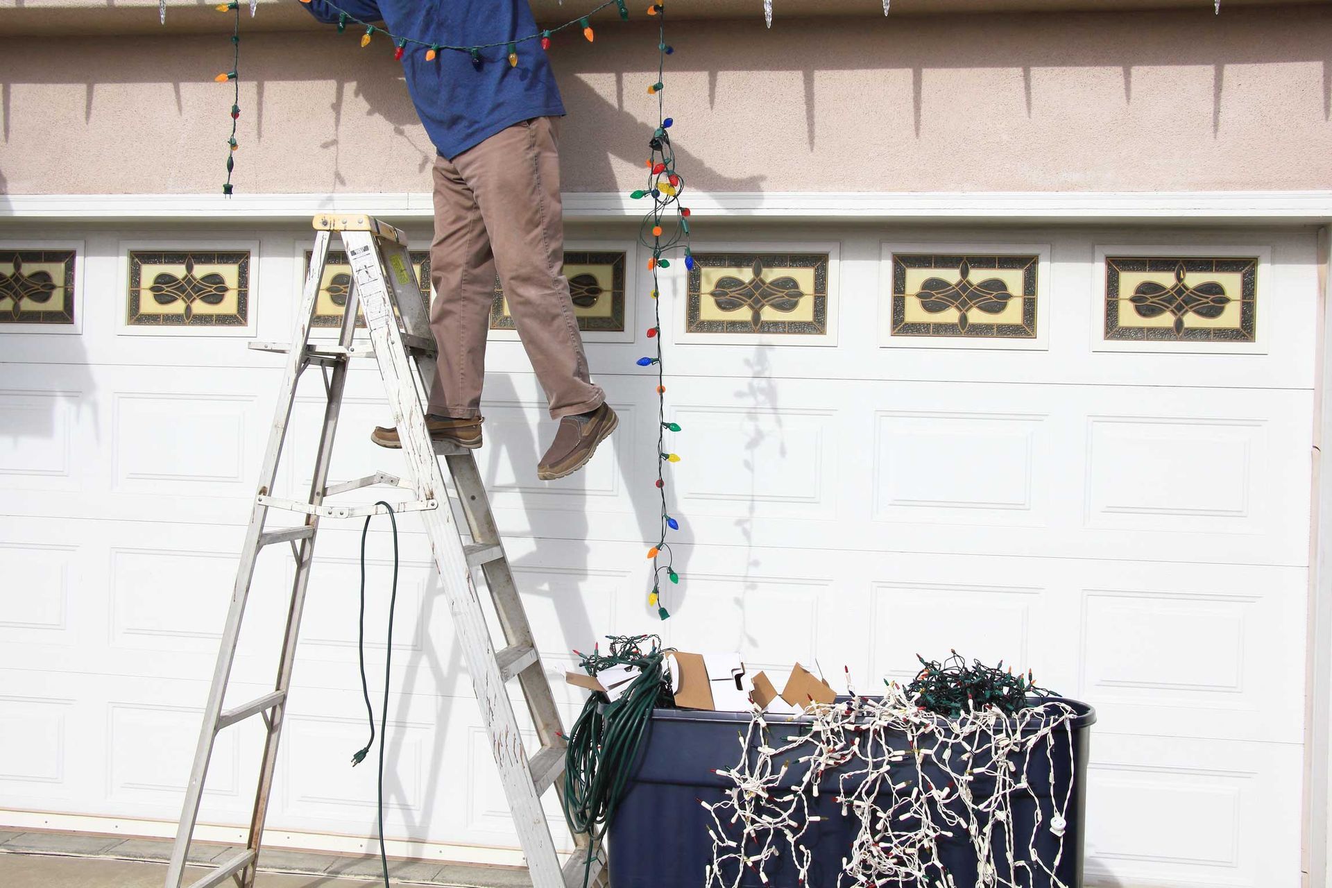 Person on a ladder hanging holiday lights above garage doors