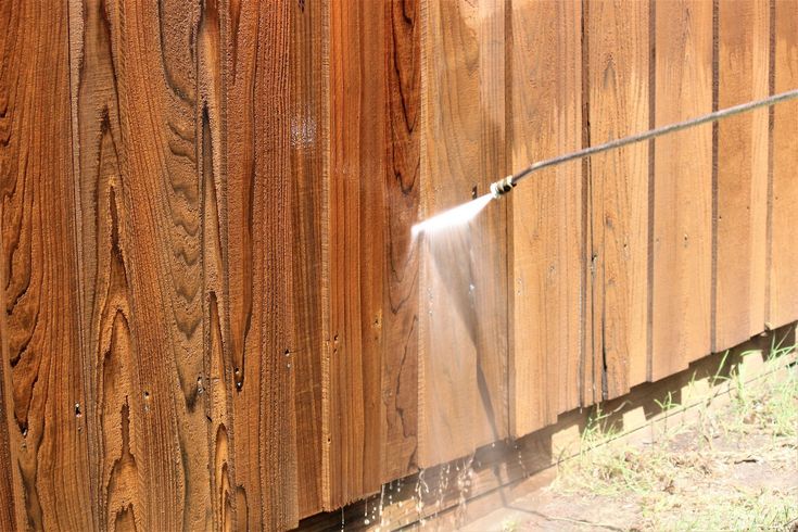Water spraying onto a wooden fence, cleaning the weathered boards.