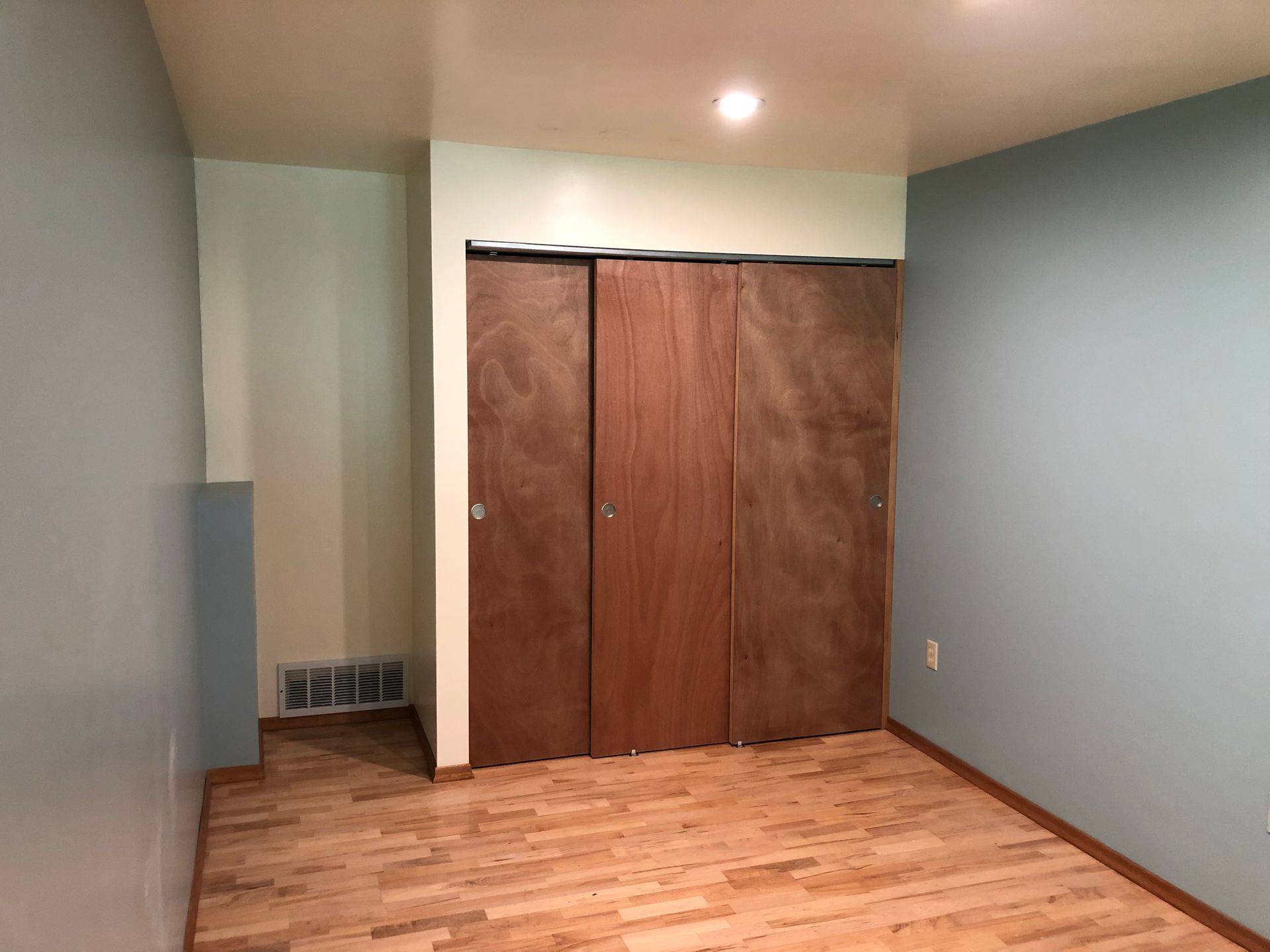 Empty room with wood floor, light blue walls, and closed brown closet doors.