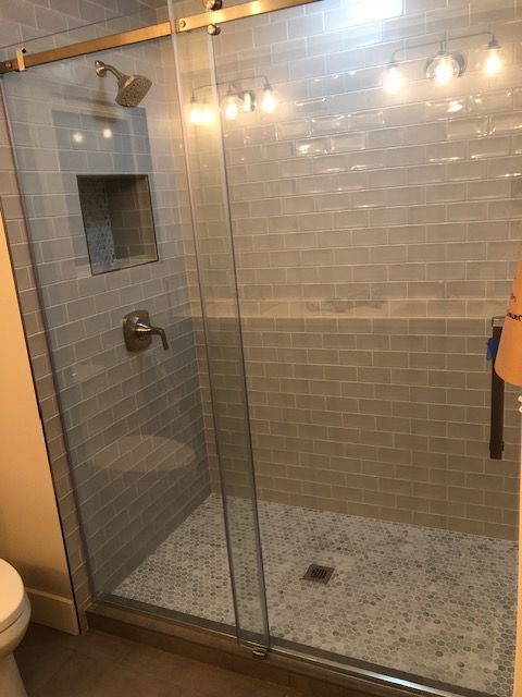 Glass shower with gray tile walls and pebble floor, lit by string lights