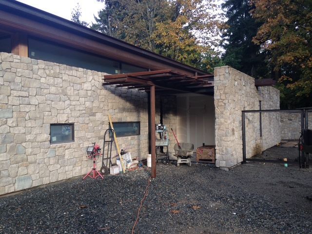 Stone house exterior with gravel driveway, covered entry, and tools leaning against the wall
