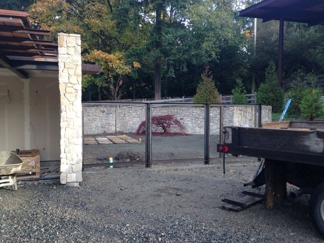Gravel yard with stone wall, covered patio, and a black trailer in the foreground