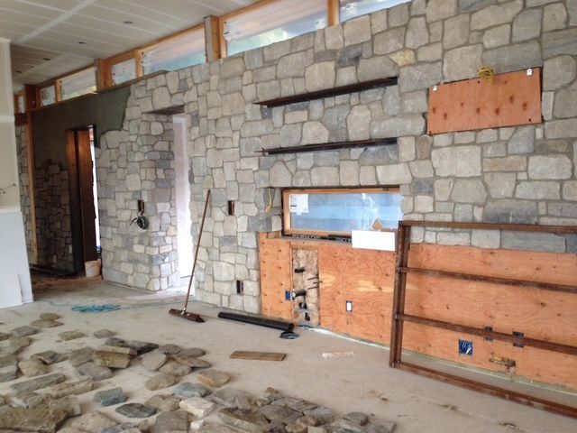 Stone fireplace wall under construction with exposed plywood and unfinished floor in a rustic room