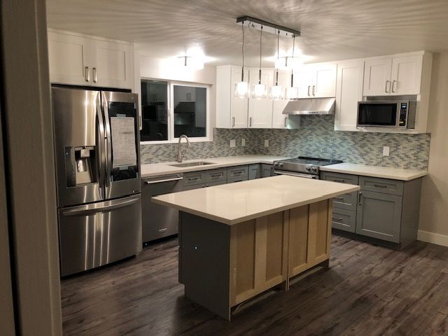 Modern kitchen with stainless steel appliances, white cabinets, gray tile backsplash, and a central island.
