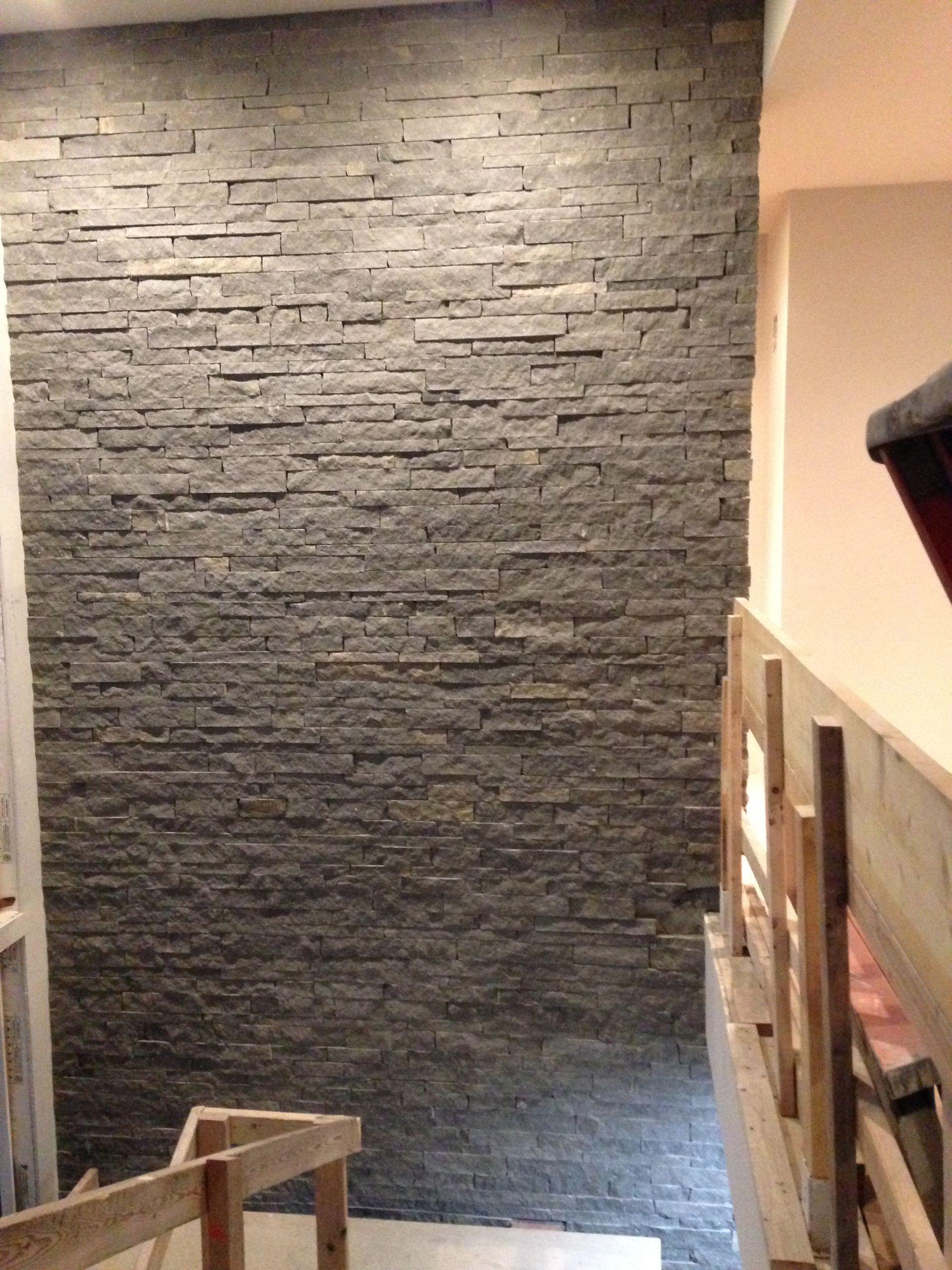 Stone accent wall in an interior stairwell with wooden railing and beige walls.