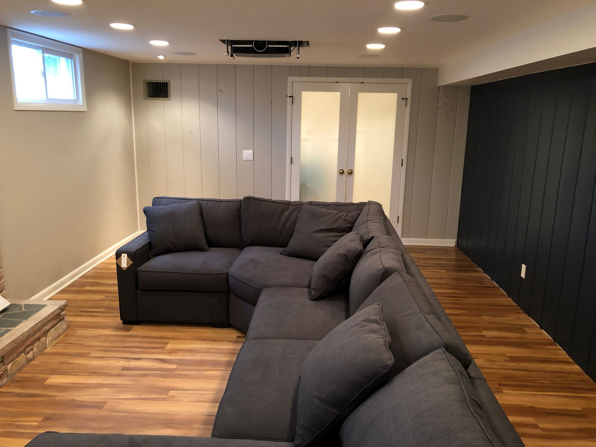 Basement living room with a dark gray sectional sofa, wood floor, and white double doors.