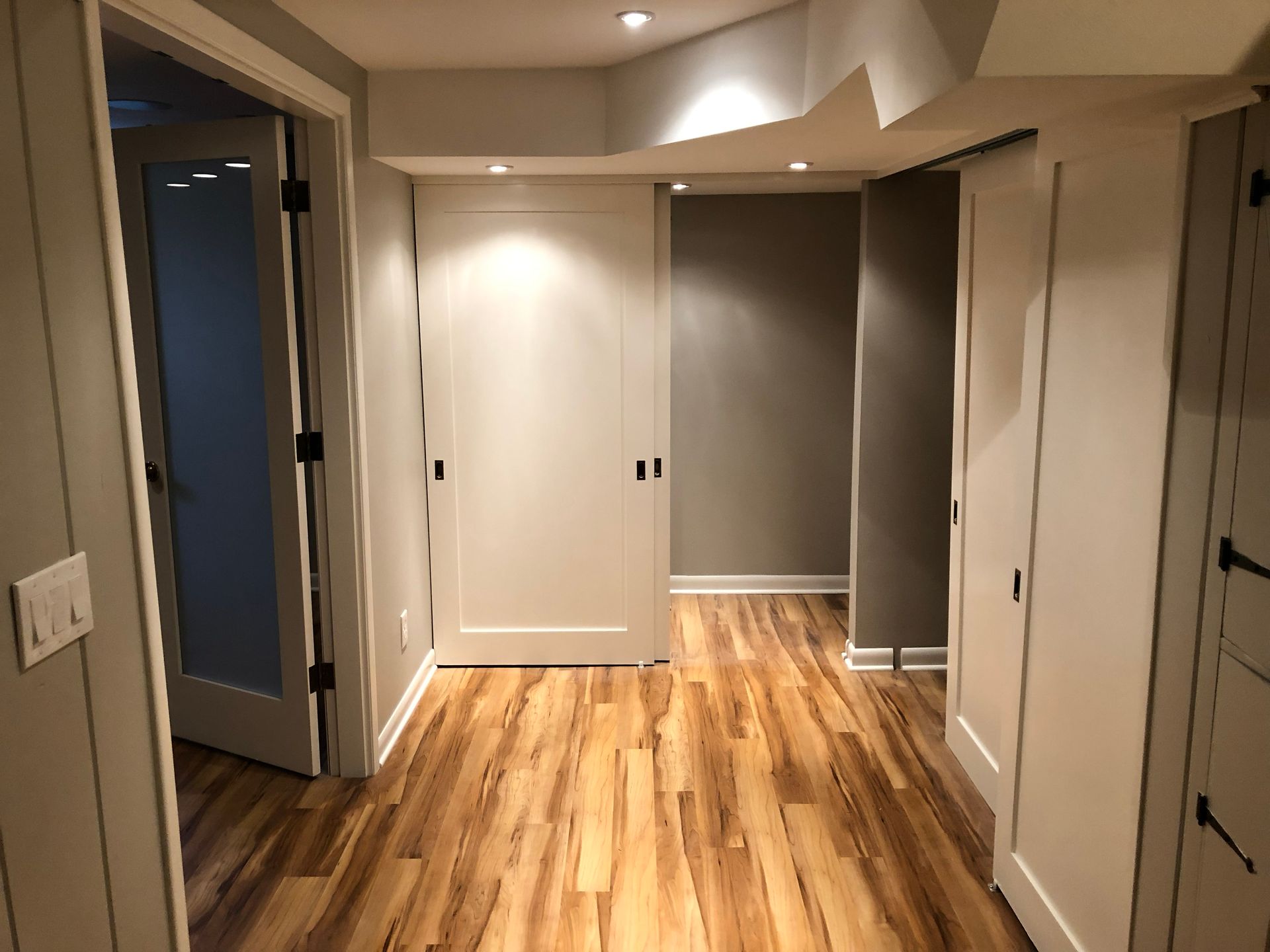 Empty hallway with wood floors, beige walls, and open doors leading to other rooms.