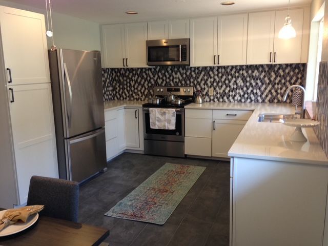 Modern kitchen with stainless steel appliances, white cabinets, patterned backsplash, and island seating