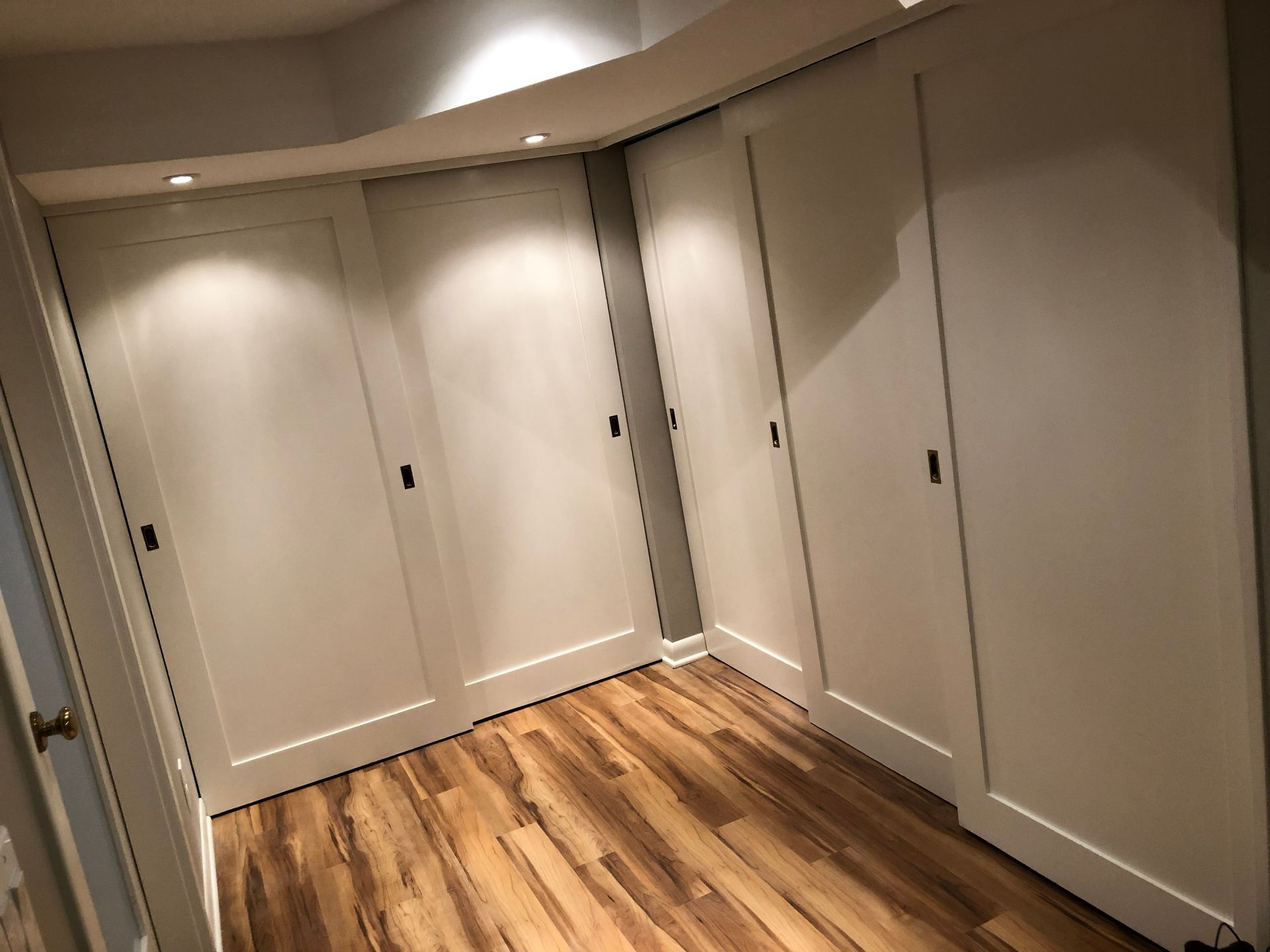 Empty hallway with white closet doors and wood flooring under warm ceiling lights
