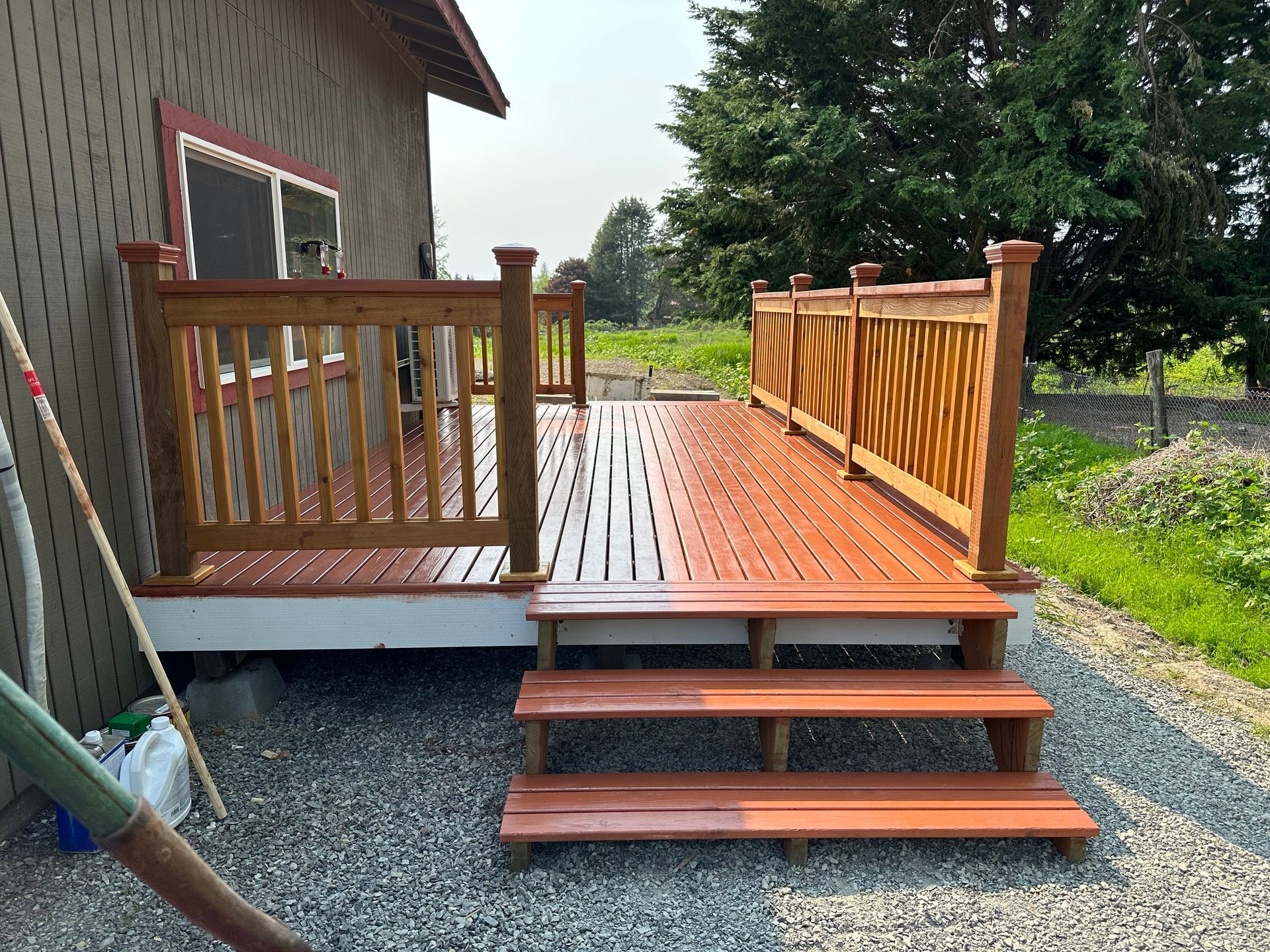 Wooden deck with railing and steps beside a house, set in a gravel yard.
