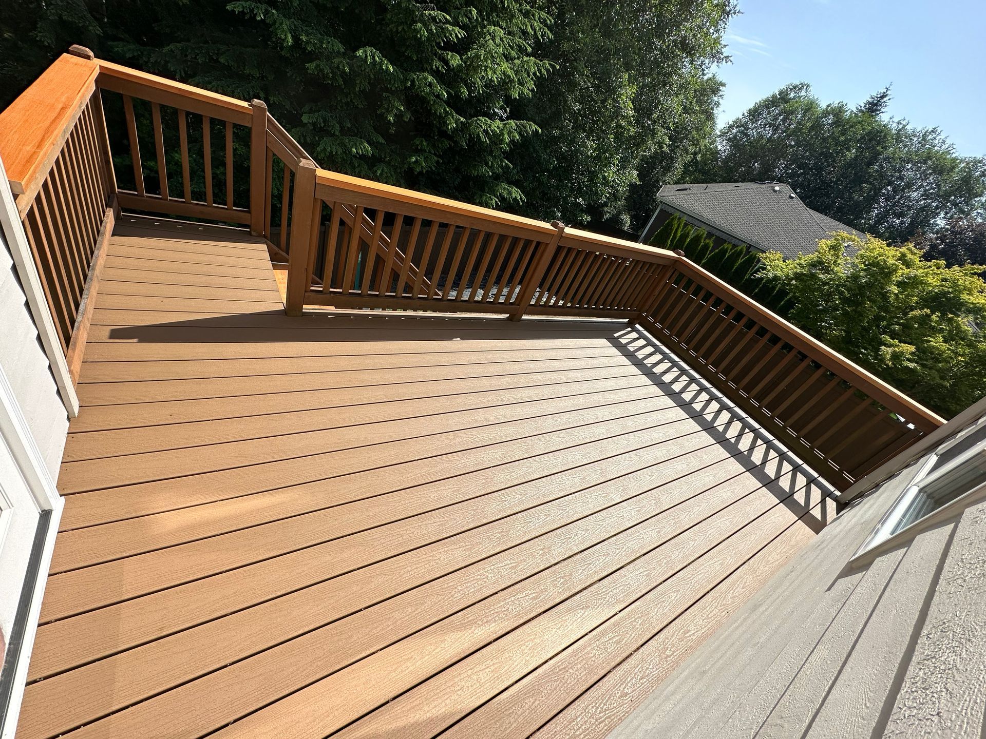 Wooden deck with railings and steps, overlooking a leafy backyard on a sunny day