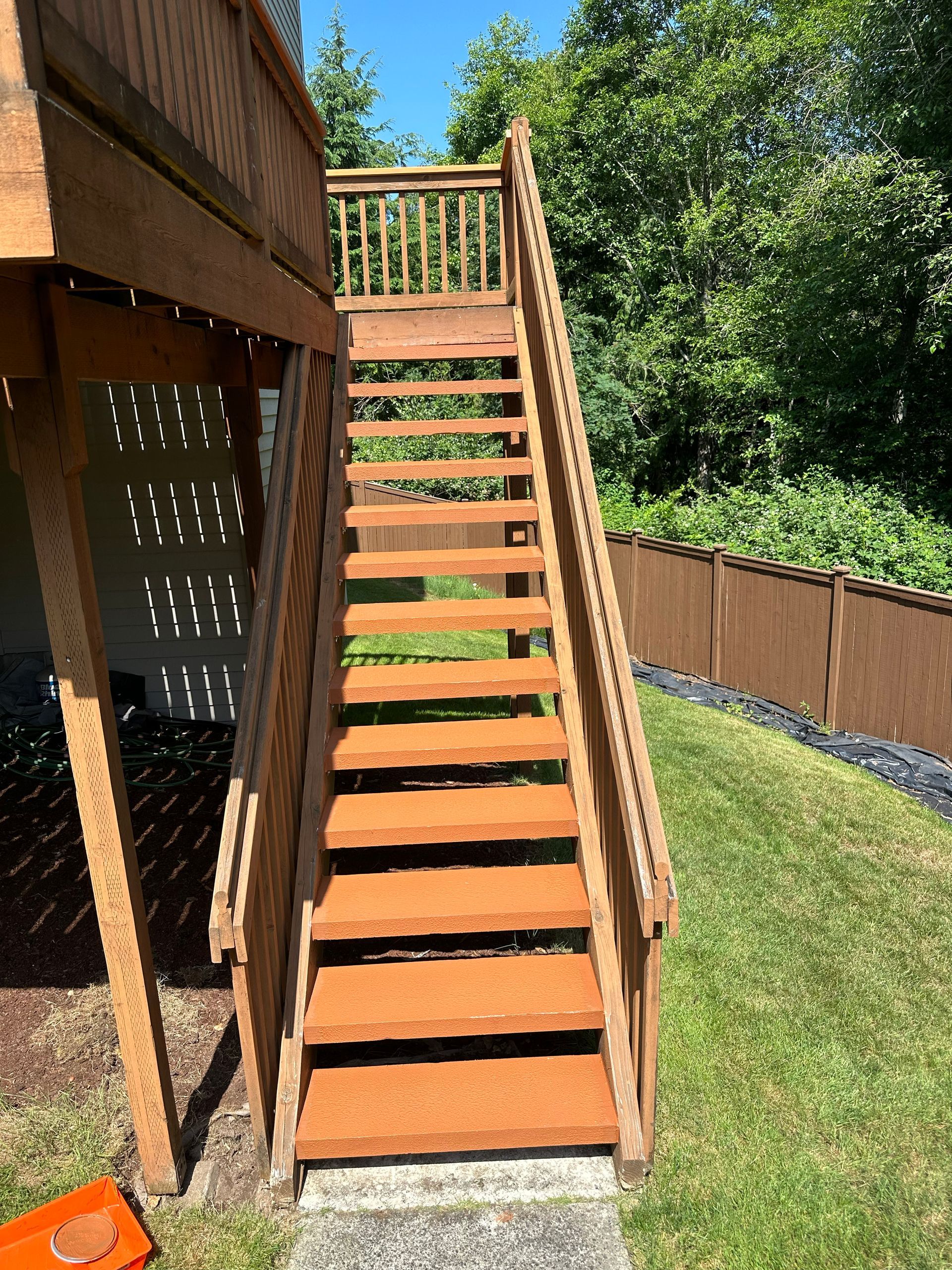 Wooden outdoor staircase with orange steps leading to a deck in a sunny backyard.