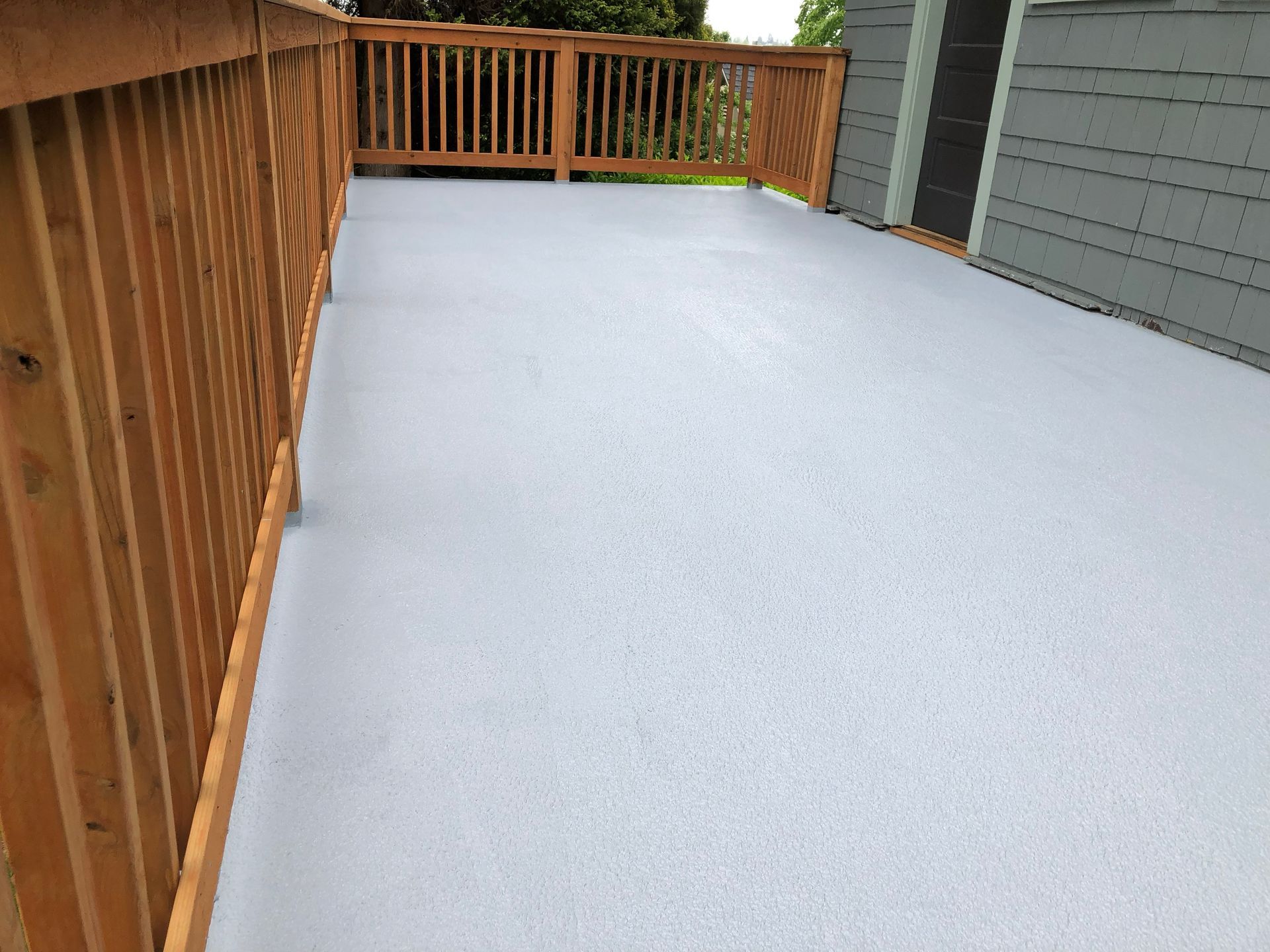 Snow-covered wooden deck with railing beside a house