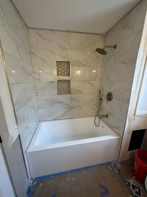 Modern white-tiled shower tub with built-in niche, chrome fixtures, and showerhead