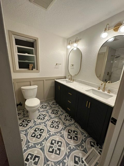 Small bathroom with patterned tile floor, black vanity, white sink, toilet, mirror, and wall sconces.