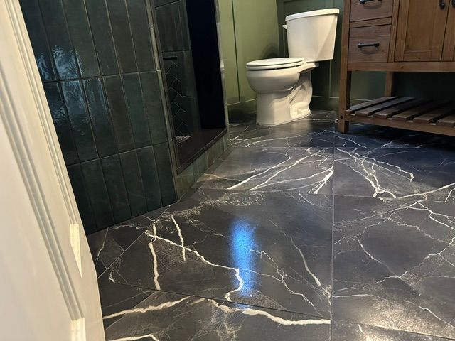 Bathroom with glossy black marble floor, white toilet, dark tiled walls, and wooden cabinet sink.