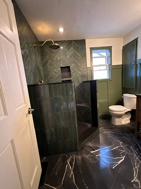 Modern bathroom with dark green tile walls, black marble floor, white toilet, and glass shower.