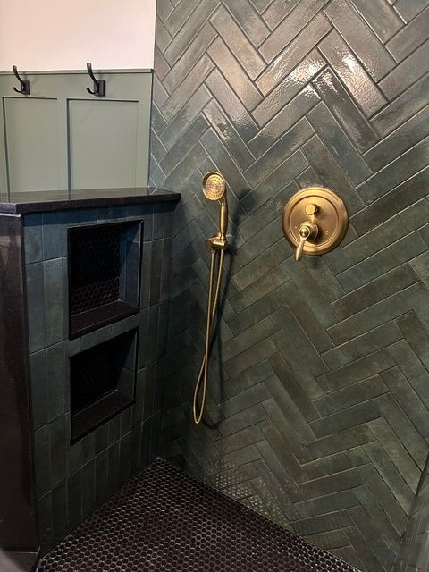 Dark green herringbone tile shower with brass showerhead and wall niche in a bathroom.
