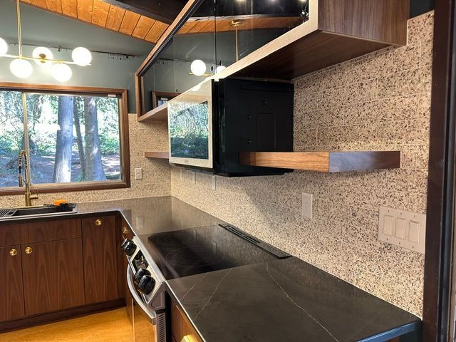 Modern kitchen with black countertops, wood cabinets, open shelves, and a window over the sink.