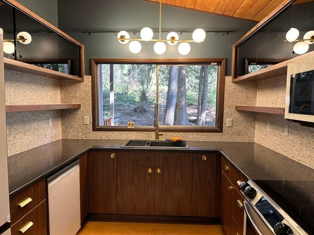 Modern kitchen with wood cabinets, open shelving, a large window, and warm ceiling lights