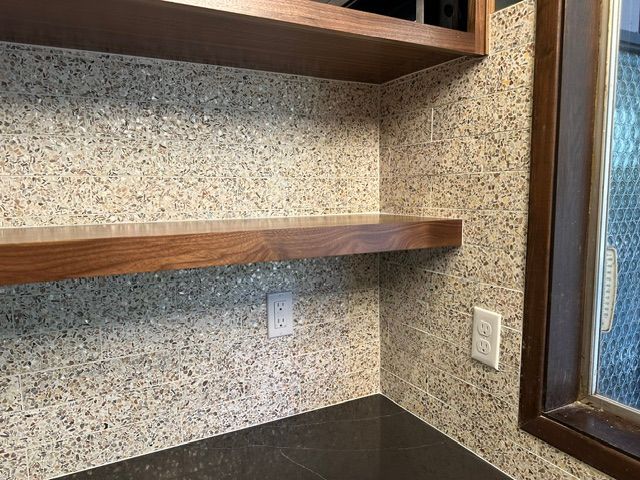 Small office nook with wood shelves, speckled wallpaper, a dark countertop, and a window on the right.