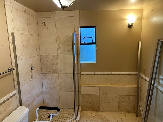 Bathroom with tiled shower, glass door, grab bars, and a built-in bench.
