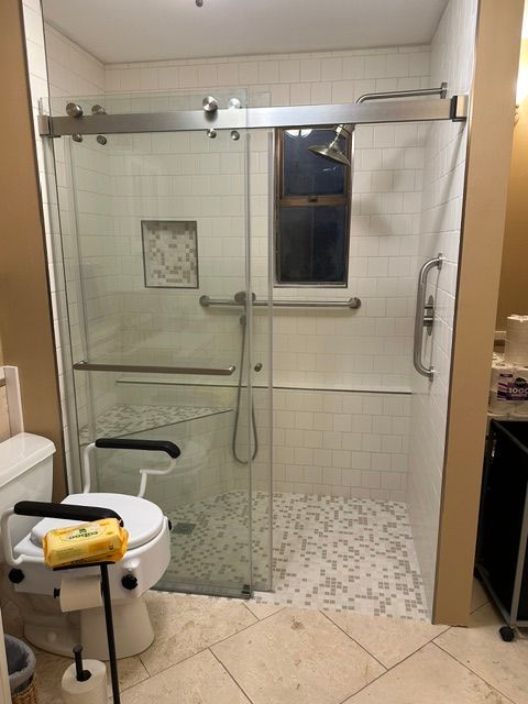 Bathroom with glass walk-in shower, tiled walls, and a toilet in the foreground.