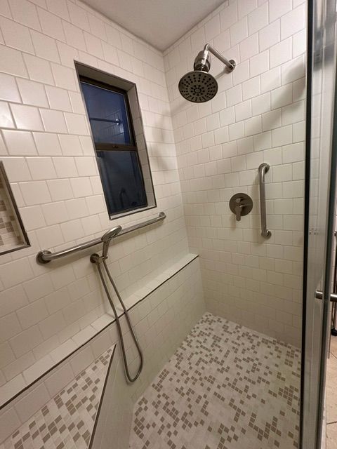 Accessible shower stall with grab bars, handheld showerhead, and tiled walls.