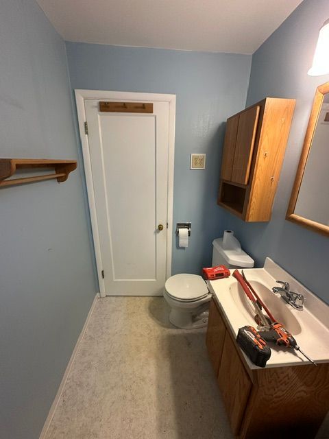 Small blue bathroom with toilet, sink, mirror, and cabinet; door at far end and narrow space.