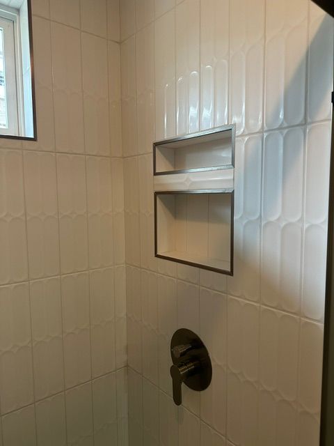 Small tiled bathroom shower wall with built-in shelf, window, and shower control valve