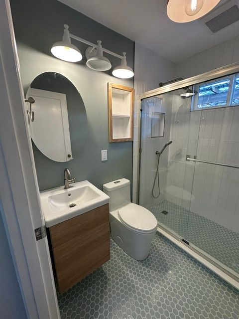 Modern bathroom with blue walls, vanity sink, toilet, and glass shower enclosure