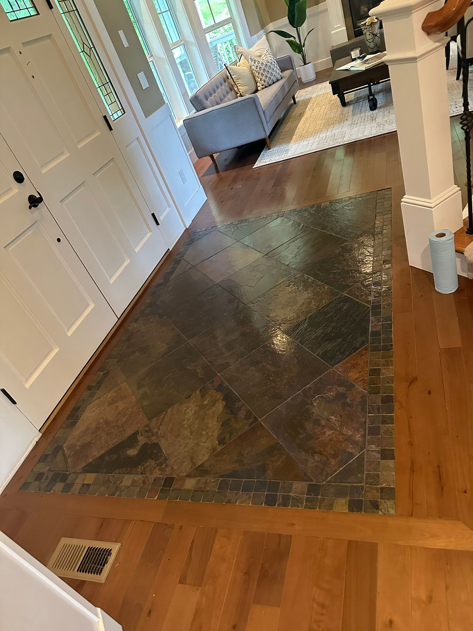 Hallway with hardwood floors, a dark rug, white doors, and a gray sofa in the background