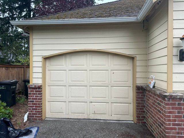 Beige garage door with brick sides and siding on a house exterior