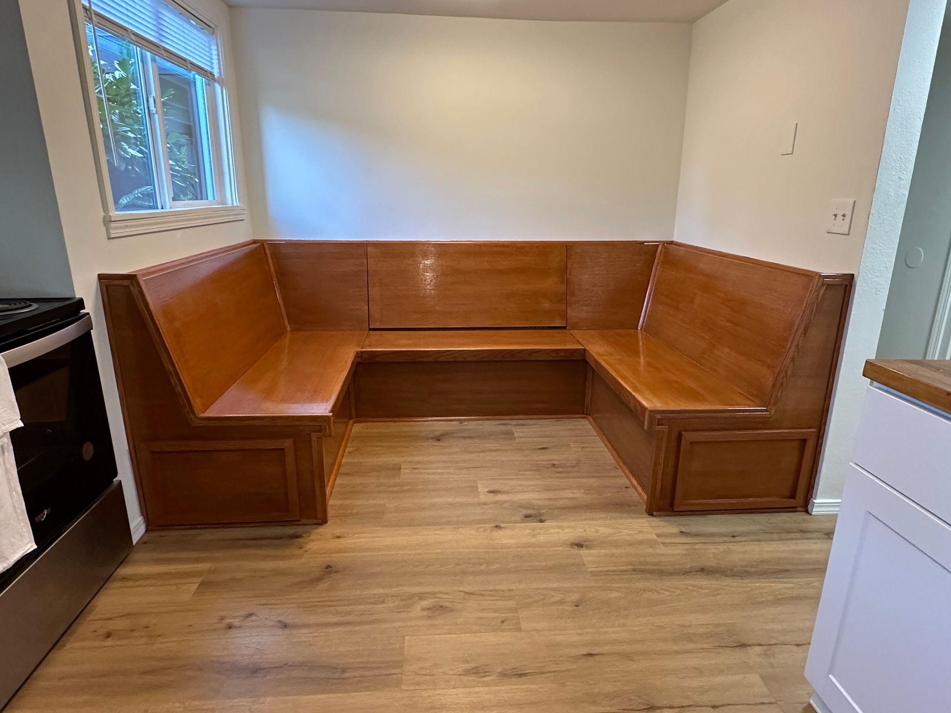 Built-in wooden corner bench seating in a small room with wood floor and windows