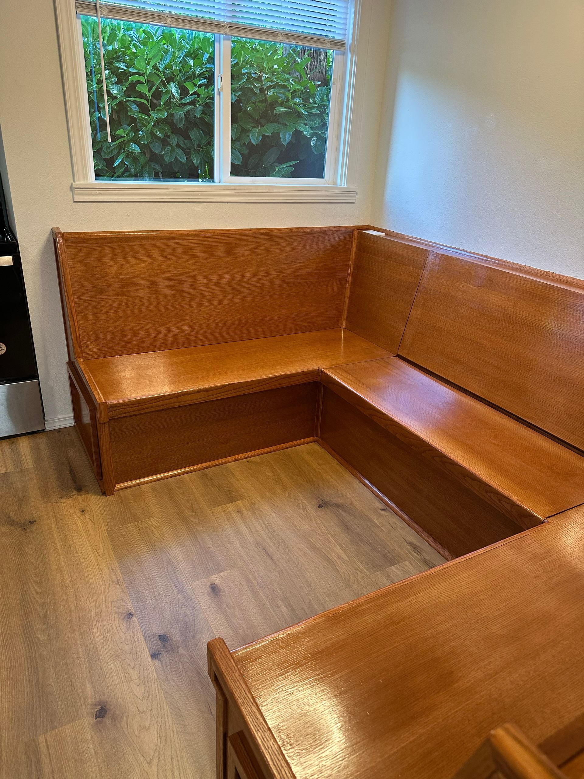 Wooden L-shaped bench seating in a small room beneath a window.
