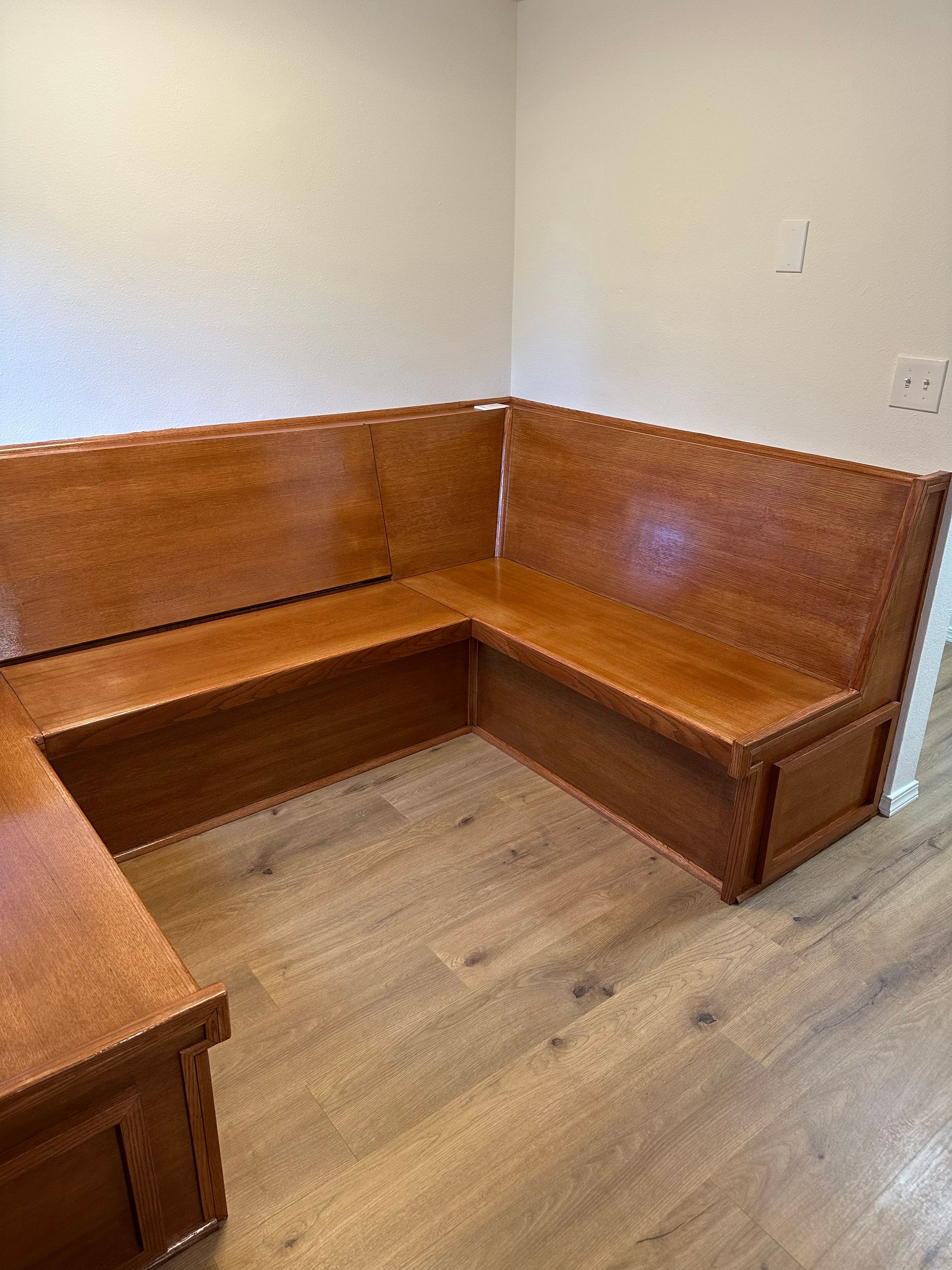 Wood-paneled corner bench seating in a small room with light wood flooring.