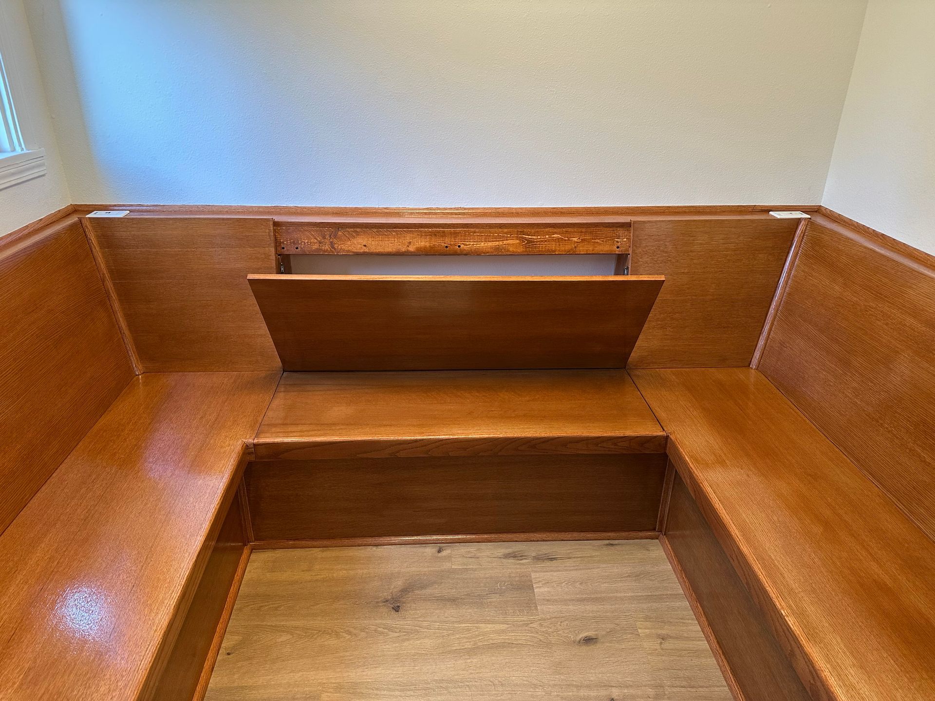 Wooden church pew interior with red-brown paneling and a central kneeler on a beige floor.