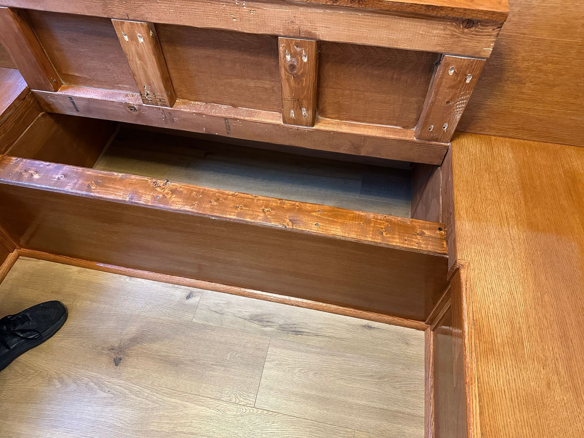 Open wooden storage compartment with hinged lid and carpeted floor visible inside
