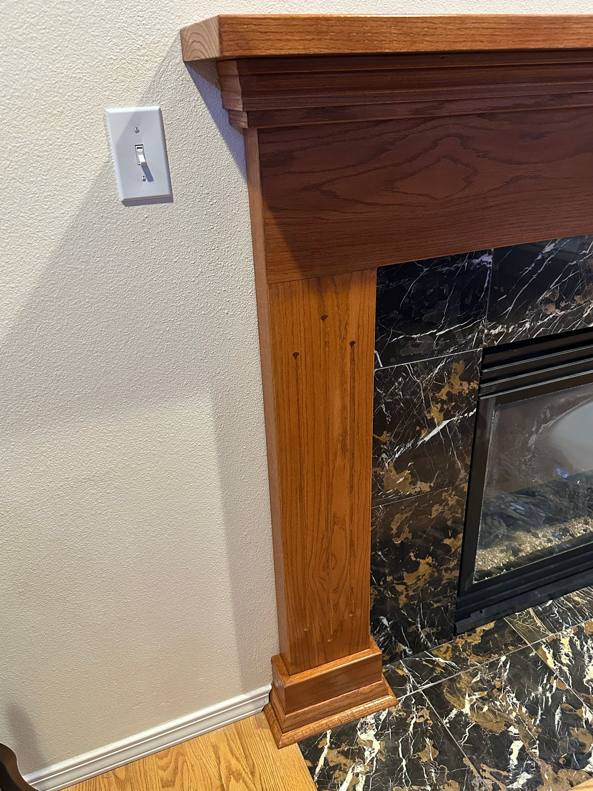 Fireplace mantel and marble surround beside textured wall with a light switch.