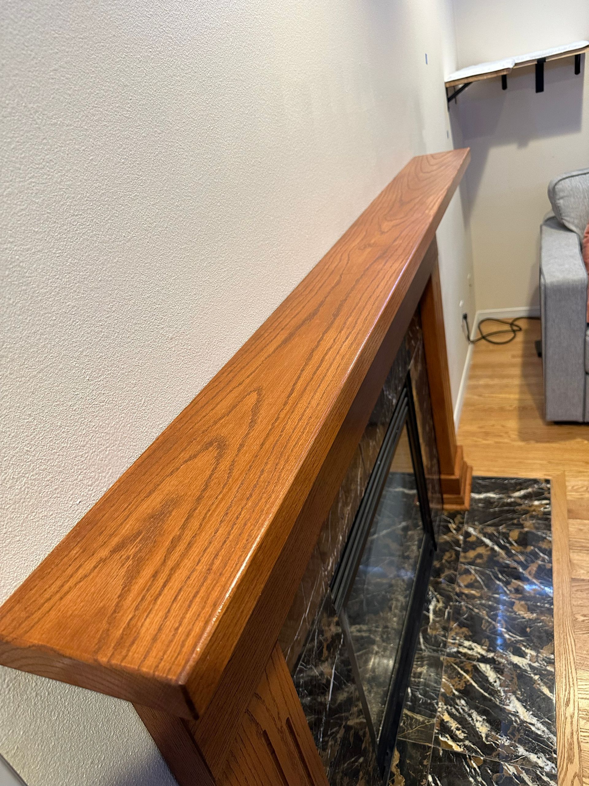 Wooden mantel shelf above a black marble fireplace in a beige living room