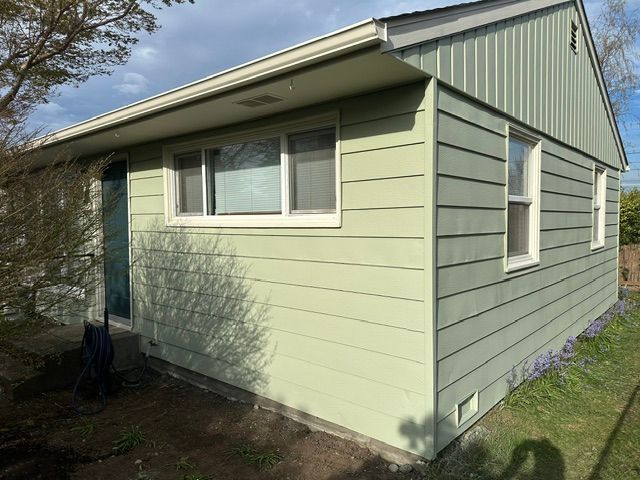 Light green house exterior with windows, white trim, and a sloped roof in a grassy yard.